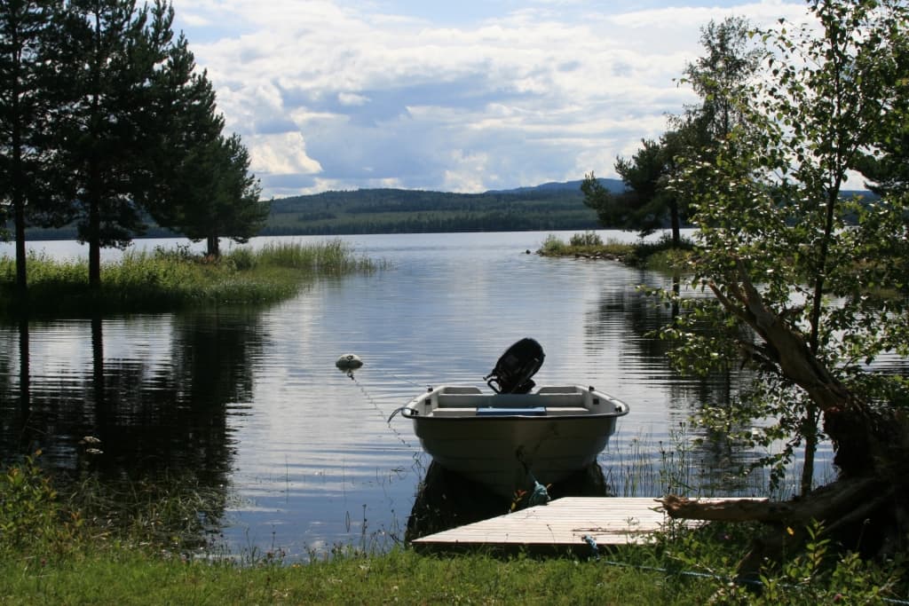 Sollerön - Ön i Siljan, Dalarna Sollerön i Siljan med brygga, båt och stilla sjövatten omgivet av skog och fjäll
